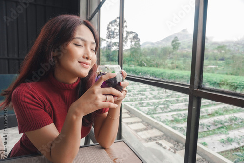 Portrait of joyful young woman enjoying a cup of tea at home. Smiling pretty girl drinking telang tea in rainy season. Free Download Portrait of joyful young woman enjoying a cup of tea at home. Smiling pretty girl drinking telang tea in rainy season. - GFXLoad