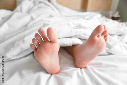 Couple feet under sheets on the bed at home. © Reezky