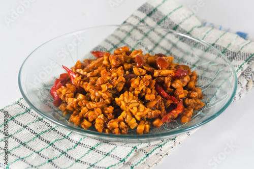 sliced tempeh fried dry with chilies and peanuts or orek tempe served on a small plate with a napkin isolated on a white background photo