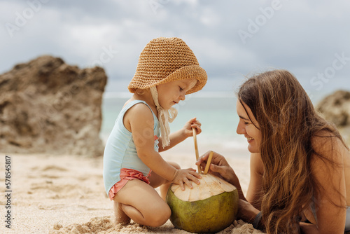 Loving mother and her daughter relaxing on the beach,  drinking coconut water. Family tropic vacation photo