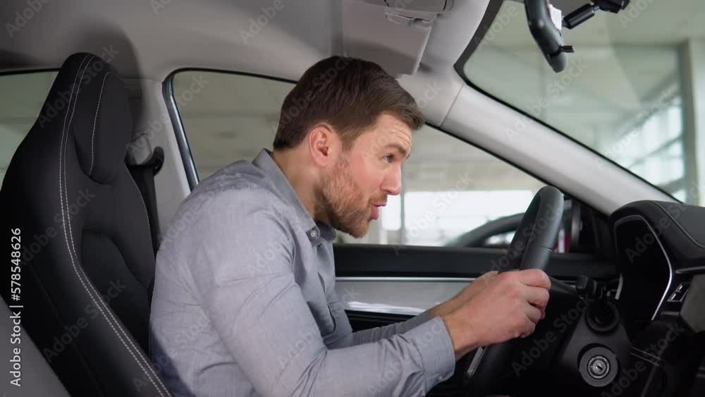 Funny buyer pretends to drive a electric car in a car dealership. Concept of happiness and expensive purchase Funny buyer pretends to drive a electric car in a car dealership. Concept of happiness and expensive purchase