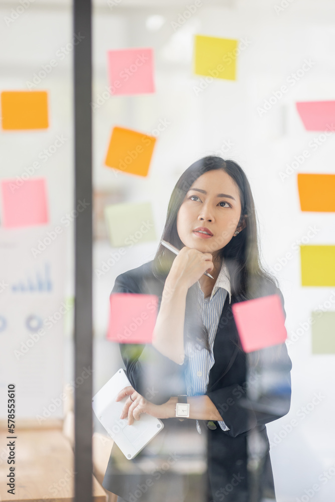 Young Serious Asian Creative team use post it notes to share idea sticky note on glass wall. Asian business people design planning and Brainstorming thinking sticky History notes concept. Young Serious Asian Creative team use post it notes to share idea sticky note on glass wall. Asian business people design planning and Brainstorming thinking sticky History notes concept.