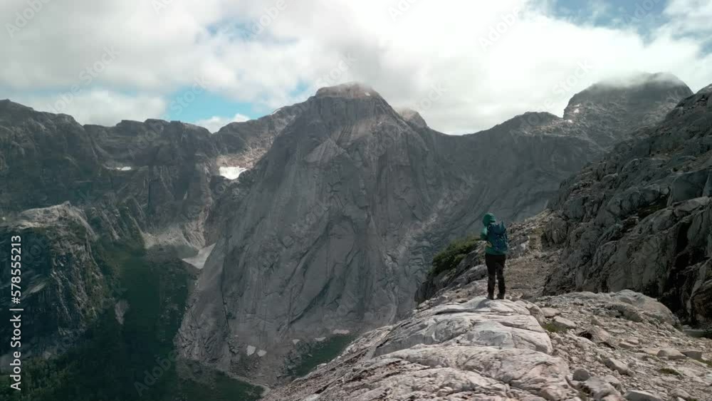 Hiker preparing himself for a trail while the drone is surrounding him letting you see a remote valley with a big mountain on the background. Hiker preparing himself for a trail while the drone is surrounding him letting you see a remote valley with a big mountain on the background.