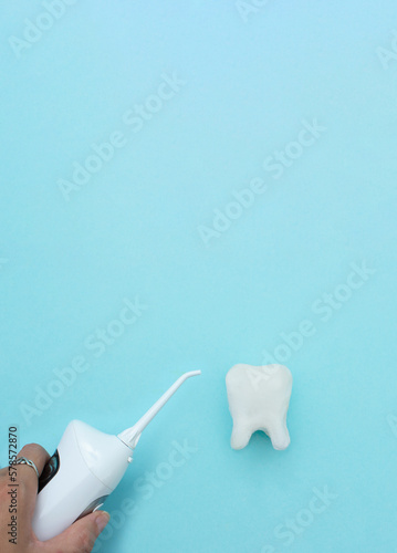 Hand hold irrigator near tooth model on blue background, professional clean teeth, teeth will good healthy. Dentist stomatology medical concept.