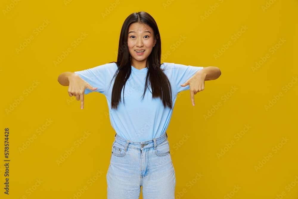 Asian woman smile with teeth hand gestures, signs and symbols on yellow background in blue t-shirt and jeans Asian woman smile with teeth hand gestures, signs and symbols on yellow background in blue t-shirt and jeans