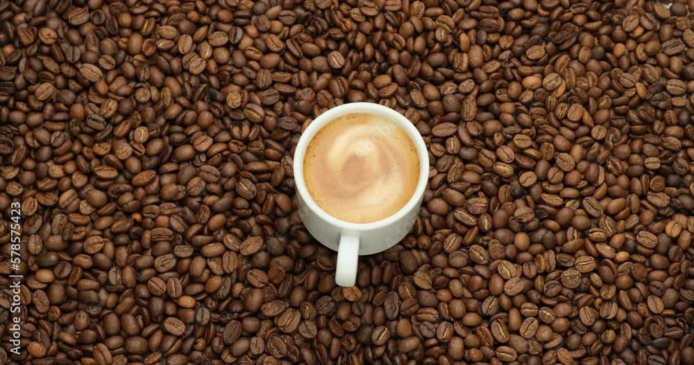Ceramic cup of hot black coffee with a rotating background of fresh roasted coffee beans Ceramic cup of hot black coffee with a rotating background of fresh roasted coffee beans