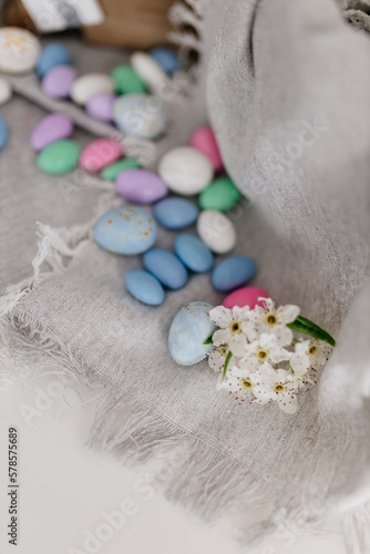 Multi-colored pastel small eggs and a blossoming pear branch lie on a linen napkin.  Easter spring background