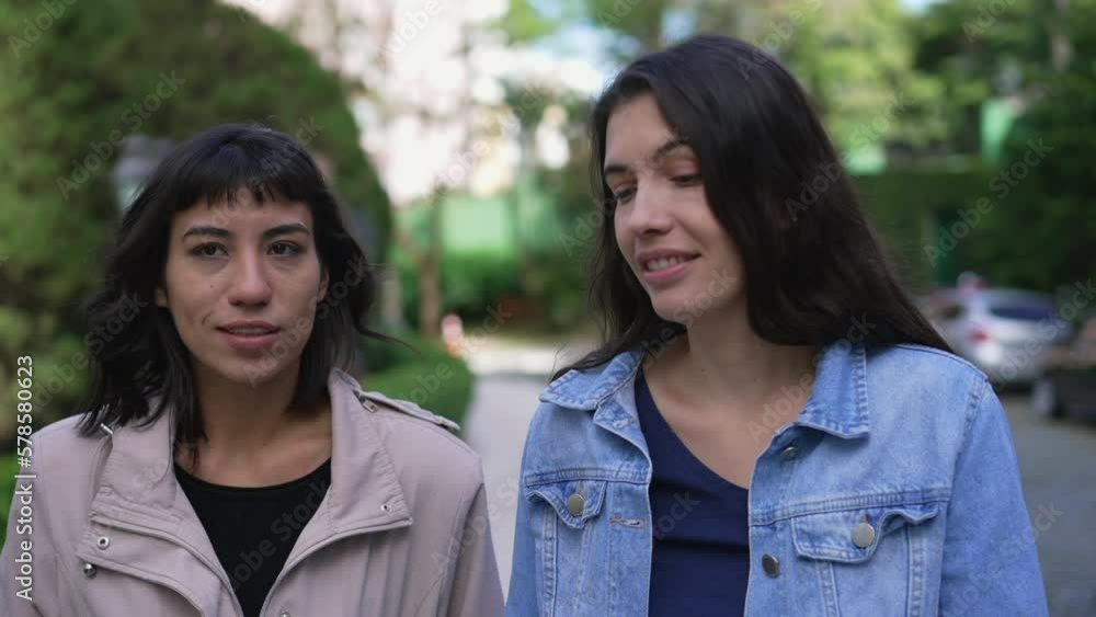 Two young women friends in conversation outside while walking forward Two young women friends in conversation outside while walking forward