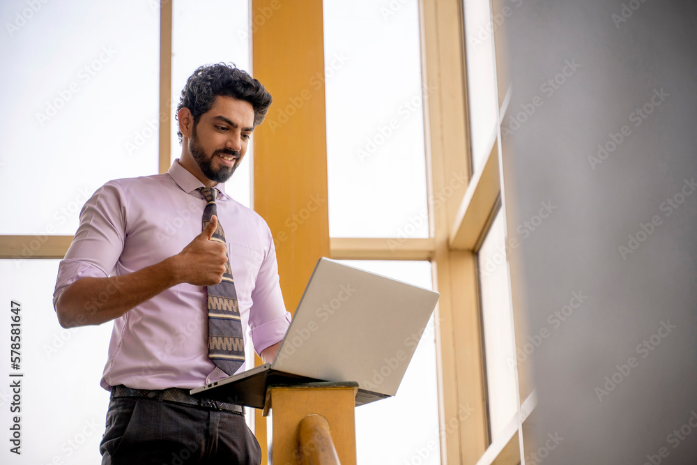 Indian manager or corporate employee using laptop and showing thumps up Indian manager or corporate employee using laptop and showing thumps up