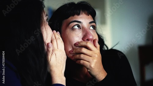 Women sharing rumor whispering SECRET to friend ear. Person reaction with SHOCK and UNBELIEF to NEWS photo