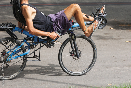 Boy in Shorts and Flip-Flops riding a Particular bicycle in a Lying down Position and with the Handlebars along the Sides