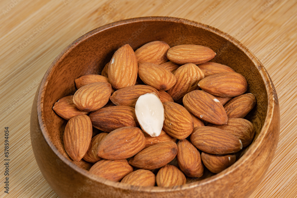 Almond nuts in wooden bowl on wooden background close up. Product rich in minerals and vitamins. Almond kernels. Healthy skin and hair and natural healing oil treatment Almond nuts in wooden bowl on wooden background close up. Product rich in minerals and vitamins. Almond kernels. Healthy skin and hair and natural healing oil treatment