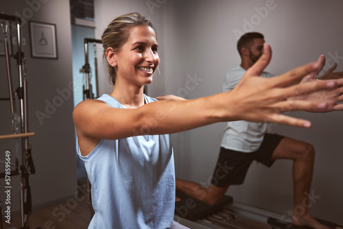 Young woman and man exercising in a gym with personal trainer on pilates machine.