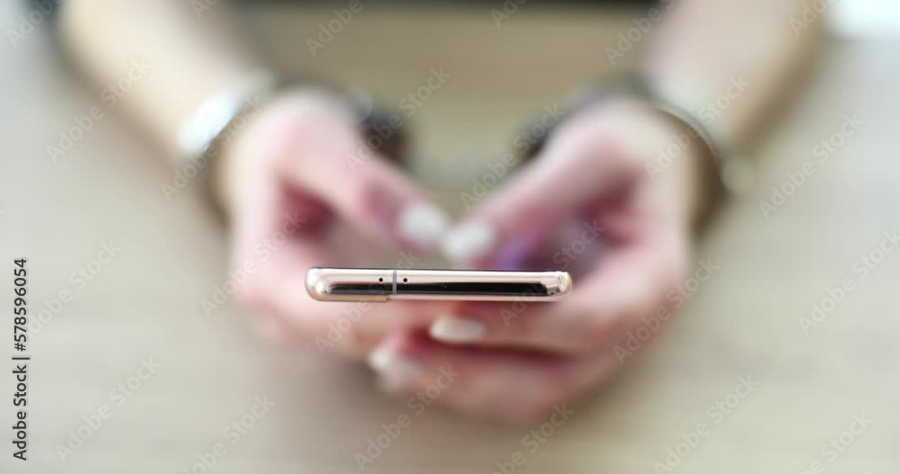 Female hands in handcuffs hold modern smartphone Female hands in handcuffs hold modern smartphone