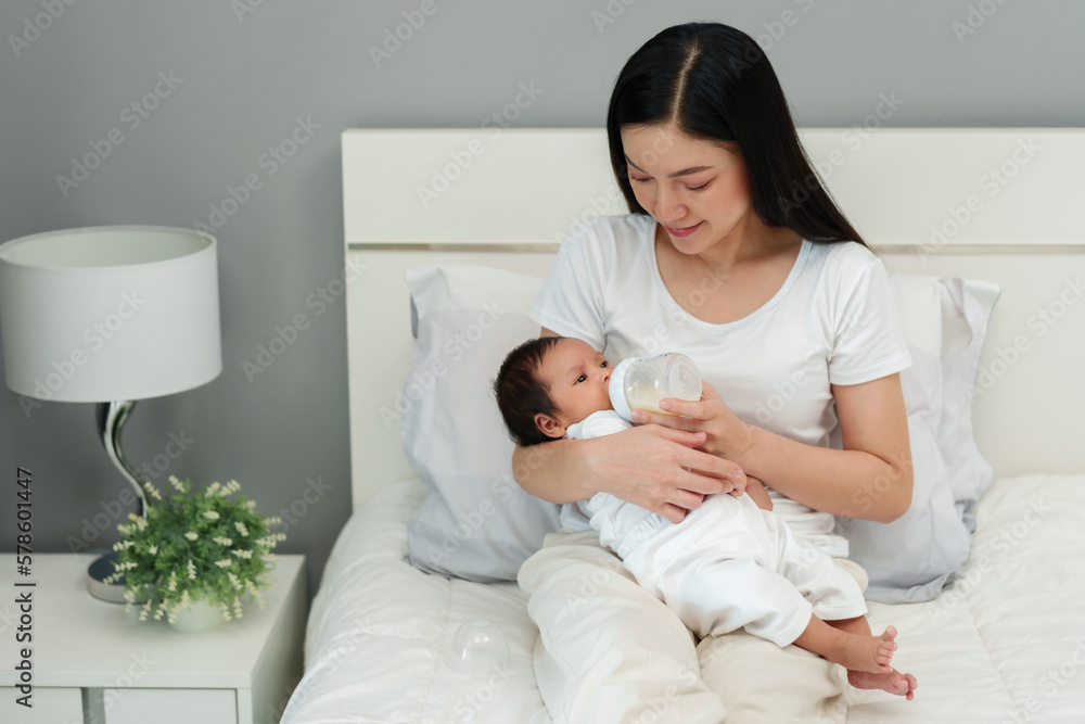 mother feeding milk bottle to her newborn baby on bed mother feeding milk bottle to her newborn baby on bed