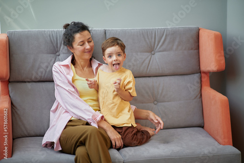 Portrait of a caucasian female playing with small kid sitting on a sofa at home. Family time together concept. High quality vertical photo