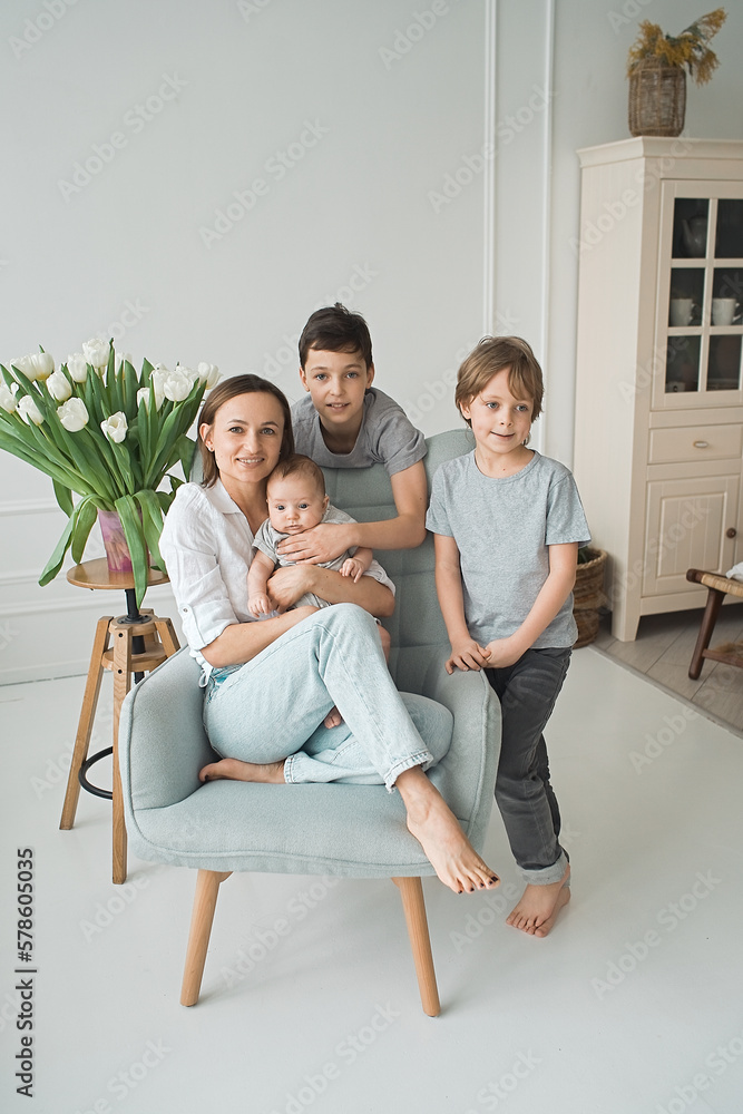 Portrait of smiling mother with
three sons sitting on the couch and looking at the camera, happy parents hugging children, big family posing for a photo at home