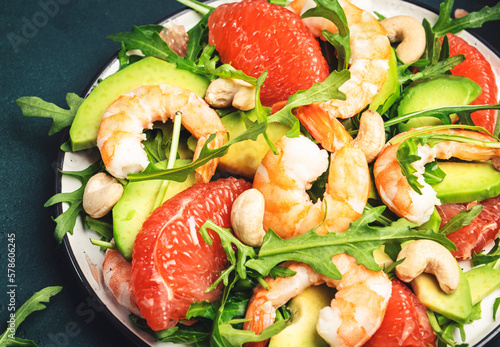 Seafood salad with shrimps, avocado, grapefruit, arugula and cashews. Dark kitchen table background, top view, close-up
