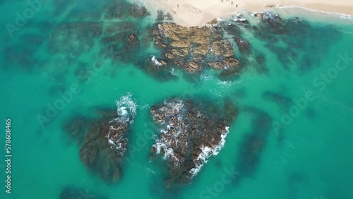 Aerial view looking down at rocky coastline with waves crashing and tropical blue water photo