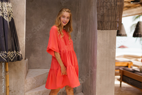 Pretty smiling blond woman in summer red dress poaing  ib beautiful tropical resort. Vacation mood. photo