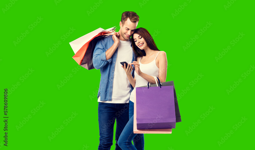 Love, holiday sales, shop, retail, consumer concept - happy couple holding shopping bags, looking at mobile phone, isolated green chroma key background. Love, holiday sales, shop, retail, consumer concept - happy couple holding shopping bags, looking at mobile phone, isolated green chroma key background.