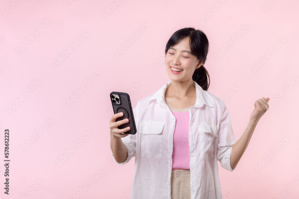 Pretty young asian woman showing success, victory hand gesture while receiving great news from smartphone on pink background. Happy technology, mobile phone advertisement, online application concept Pretty young asian woman showing success, victory hand gesture while receiving great news from smartphone on pink background. Happy technology, mobile phone advertisement, online application concept