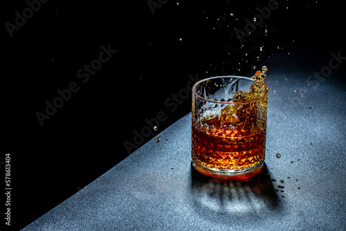 Quadro su tela One glass of cognac or whiskey with ice cubes, Freeze motion splash drops of str