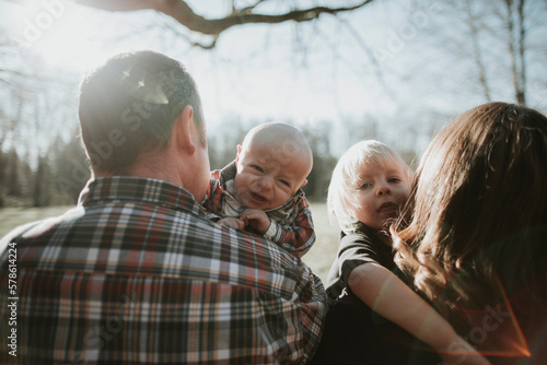 Baby and toddler look over shoulder of their parents. photo