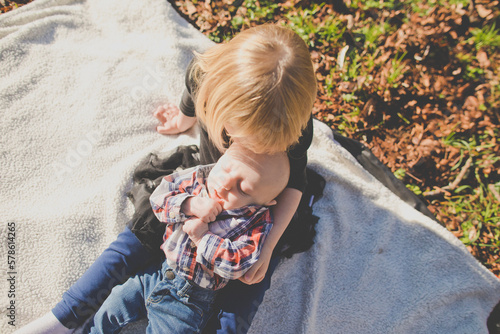 Sister holds her brother while on picnic blanket outside at park photo