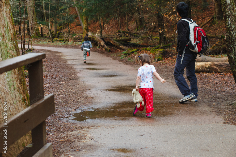 A father goes on a hike with his children down a pathway in the woods A father goes on a hike with his children down a pathway in the woods