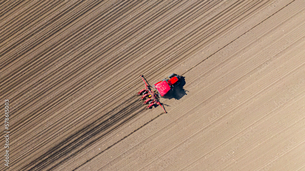 Aerial top view of tractor as dragging a sowing machine over agricultural field, farmland