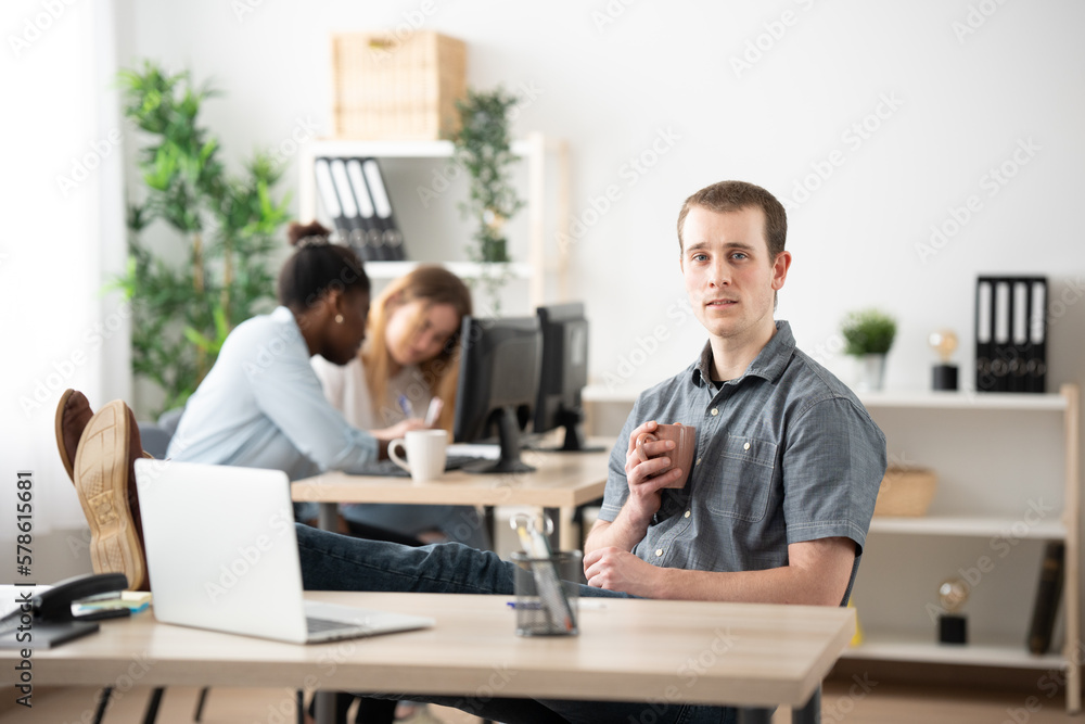 Portrait of handsome young man relaxing in the office holding a cup of coffee.