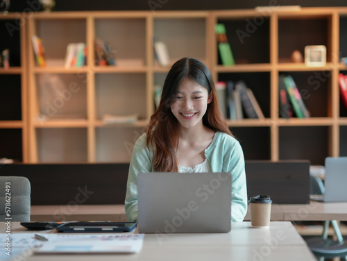 Happy young asian businesswoman sitting with laptop in office.