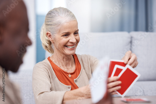 Playing cards, game and a senior woman in a retirement home having fun while sitting in a living room. Card games, happy and gambling with senior friends in a house to play poker or relax together