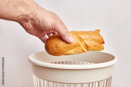 A piece of stale bread is thrown into the trash. Disposal and recycling of food waste.