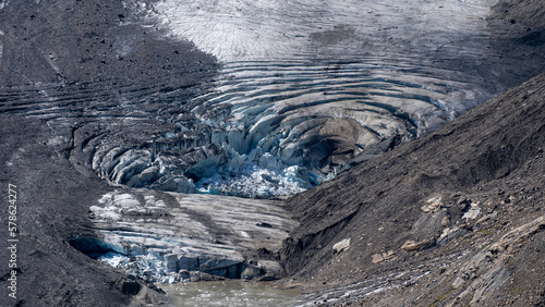 Ice of a melting glacier, showing circular cracks, in a rocky valley in an alpine mountain area