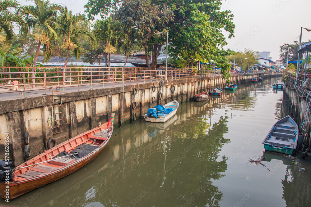 Naklejka premium A klong or river channel with fishing boats, buildings and house fronts in Thailand Asia