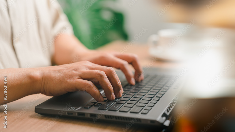 Closeup image of a young man working and typing on laptop computer keyboard on wooden table in the cafe. Closeup image of a young man working and typing on laptop computer keyboard on wooden table in the cafe.