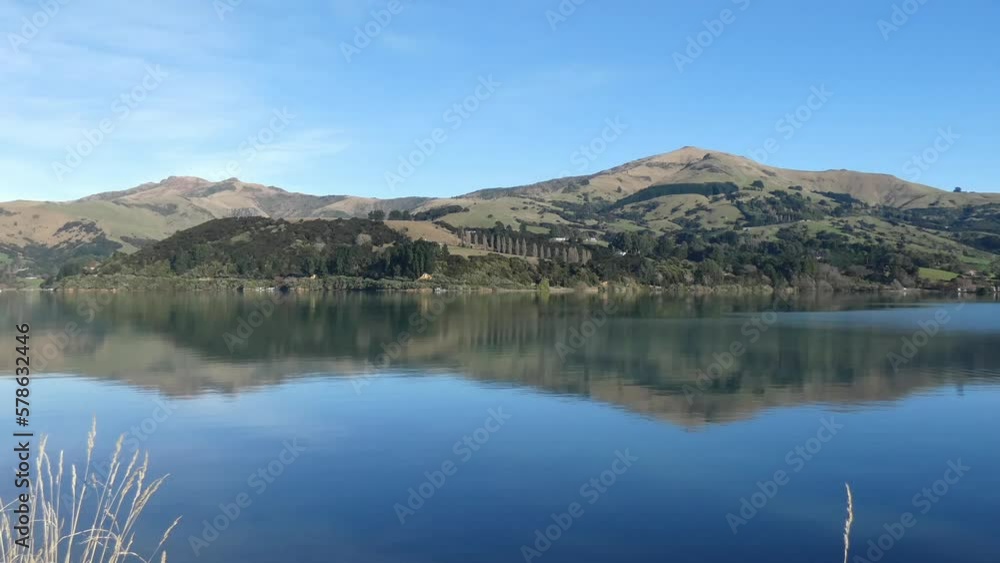 Ripples of water flow slowly across reflection of hills on a clear, calm morning - French Farm Bay, Akaroa Harbor (New Zealand) Ripples of water flow slowly across reflection of hills on a clear, calm morning - French Farm Bay, Akaroa Harbor (New Zealand)