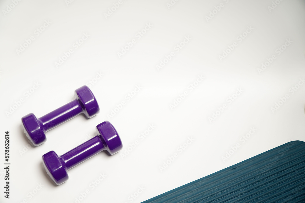 fitness accessories concept.purple dumbbell sport with blue yoga mat on white background, copy space. flat lay. view from above. fitness accessories concept.purple dumbbell sport with blue yoga mat on white background, copy space. flat lay. view from above.