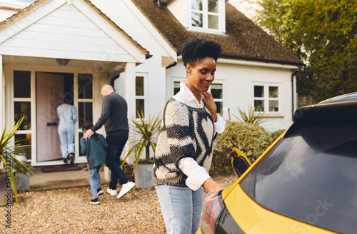 Woman charging electric car ev on driveway outside Home with family