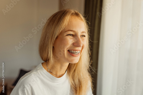 Happy laughing young woman in braces looking at window, warm positive photo