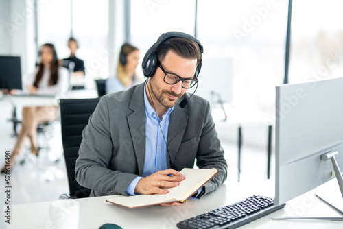 Handsome male salesperson checking clients contact phone numbers in a notebook whiling to call them and offer company products and services. photo