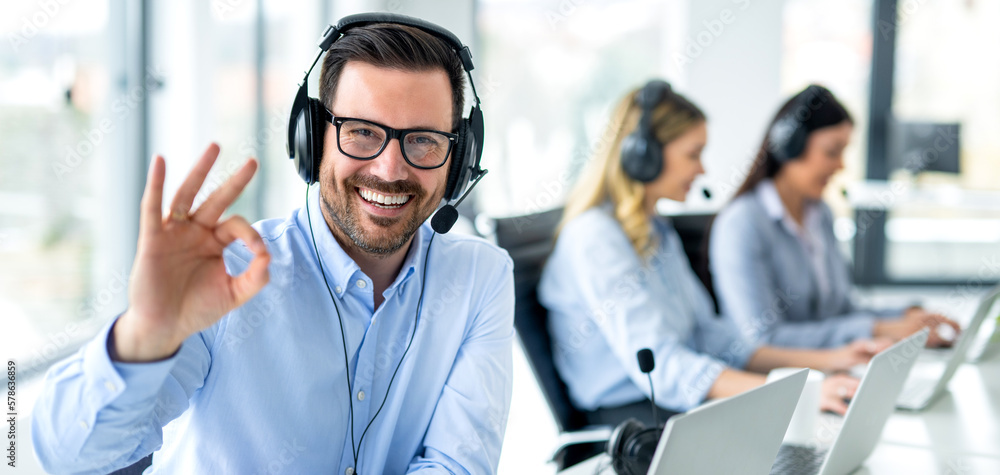 Panoramic view of handsome customer service representative showing approval sign to camera, smiling and gesturing okay at call center. Panoramic view of handsome customer service representative showing approval sign to camera, smiling and gesturing okay at call center.