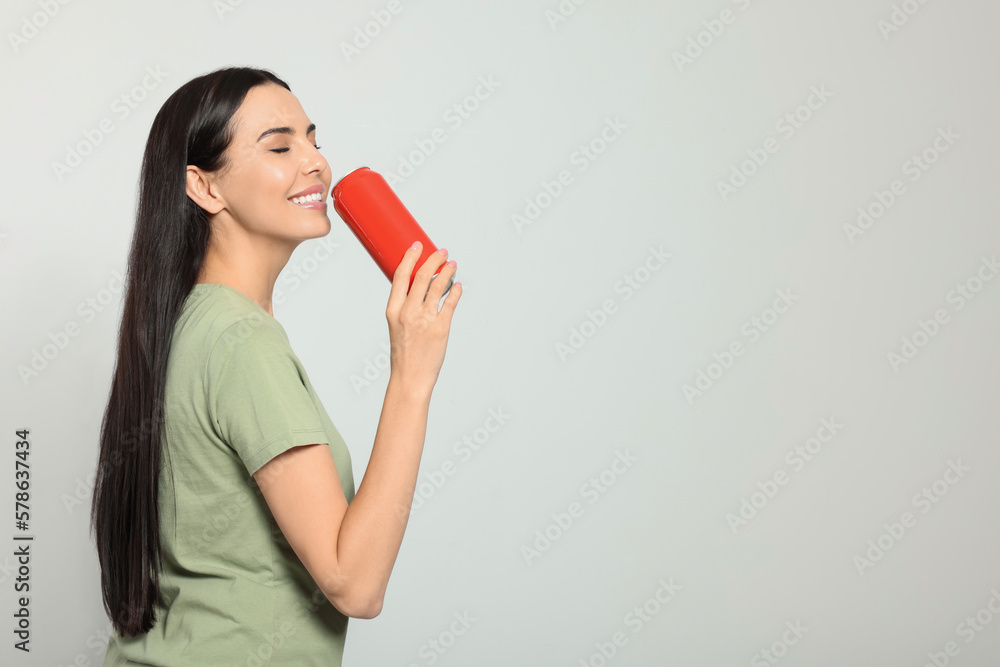 Beautiful happy woman holding red beverage can on light grey background. Space for text Beautiful happy woman holding red beverage can on light grey background. Space for text