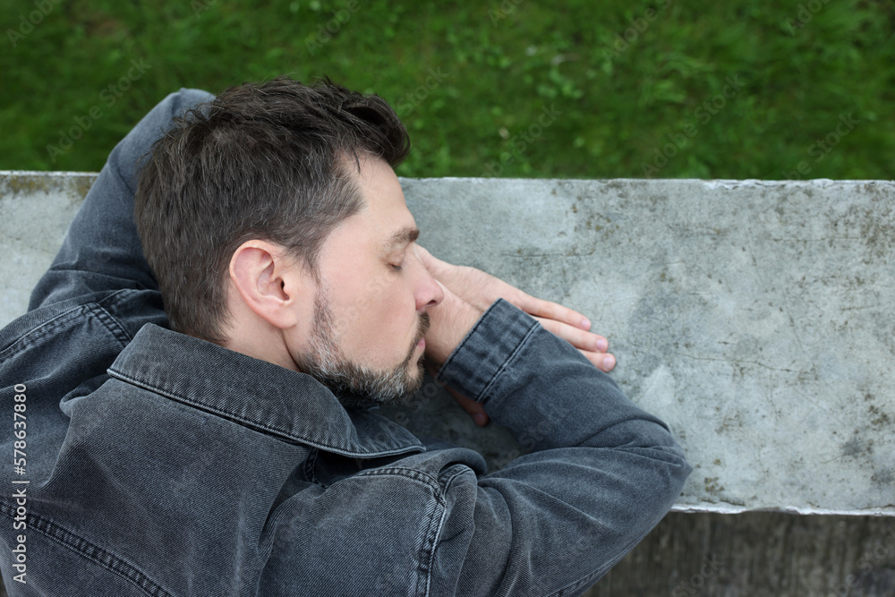Tired man sleeping on stone parapet outdoors, top view. Space for text Tired man sleeping on stone parapet outdoors, top view. Space for text