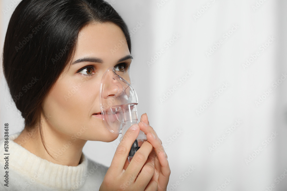 Sick young woman using nebulizer on blurred background, closeup. Space for text Sick young woman using nebulizer on blurred background, closeup. Space for text