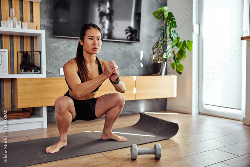 A pretty barefoot Asian woman doing a squats workout in a sportswear, at home.