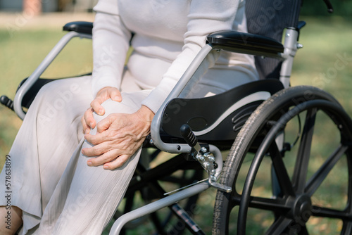 Elderly patient sitting in a wheelchair outdoor, knee pain.