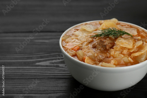Tasty cabbage soup with meat, carrot and dill on black wooden table, closeup. Space for text